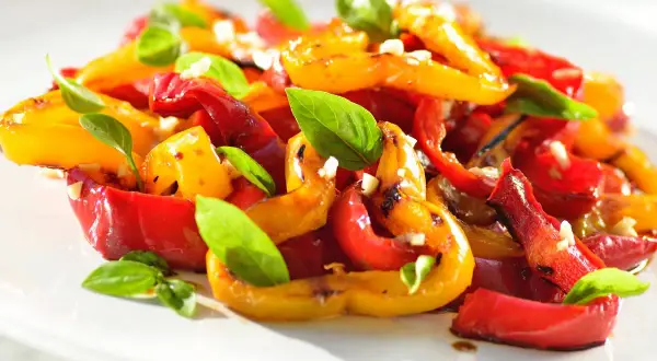Peperoni arrostiti, rossi e gialli, conditi con aglio e basilico fresco. Un'idea gustosa per le tue ricette con peperoni.