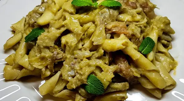Pasta con carciofi alla siciliana, un piatto saporito e profumato, guarnito con foglie di menta fresca.