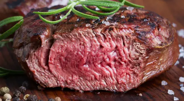 Succulenta tagliata di manzo al sangue, guarnita con rosmarino fresco e sale grosso, su un tagliere di legno.