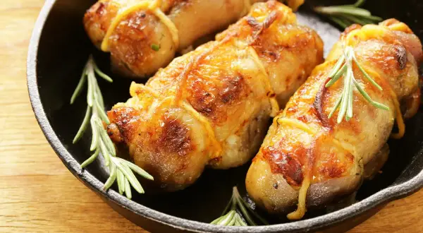 Involtini di pollo in padella, dorati e succulenti, con rametti di rosmarino fresco.