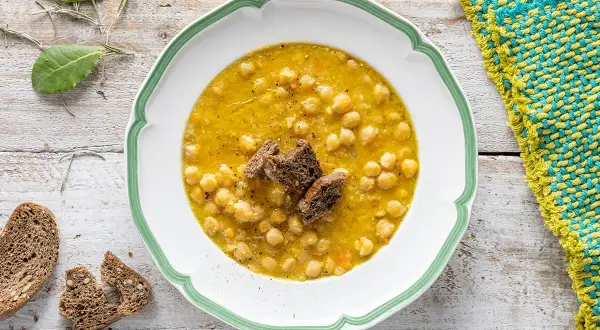 Un piatto invitante di zuppa di ceci, guarnito con crostini di pane scuro e accompagnato da fette di pane integrale.