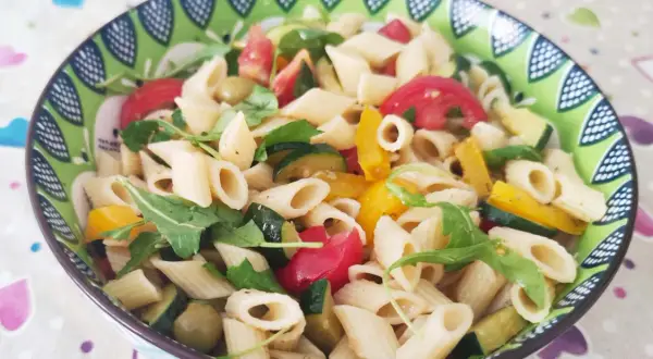 Un piatto colorato di pasta con verdure fresche: zucchine, pomodori, peperoni e rucola.