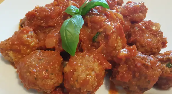 Polpette di carne morbide in un sugo rosso ricco, guarnite con foglie di basilico fresco.