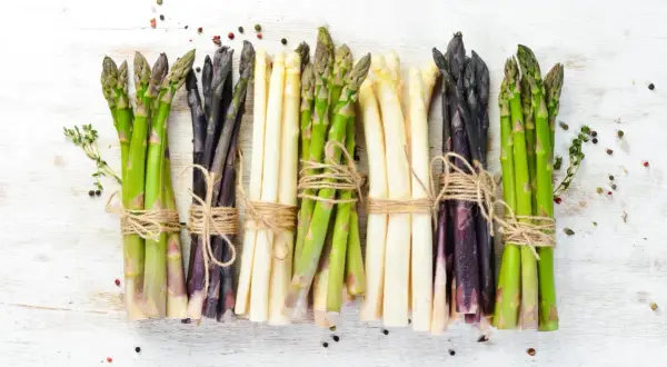 Asparagi verdi, bianchi e viola legati con spago, pronti per scoprire come cucinare gli asparagi. Spezie sparse.