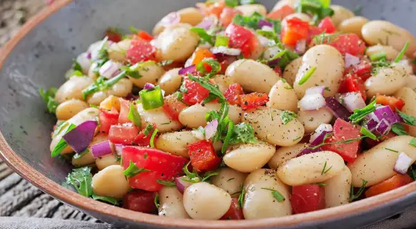 Insalata di fagioli bianchi, pomodori, cipolla rossa e erbe fresche, condita con spezie. Un piatto colorato e gustoso.