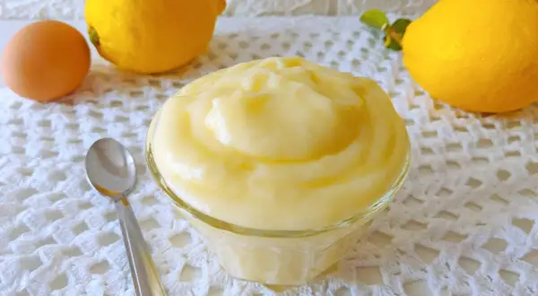 Crema pasticcera al limone, soffice e profumata, pronta per essere gustata. Accanto, un uovo e limoni freschi.