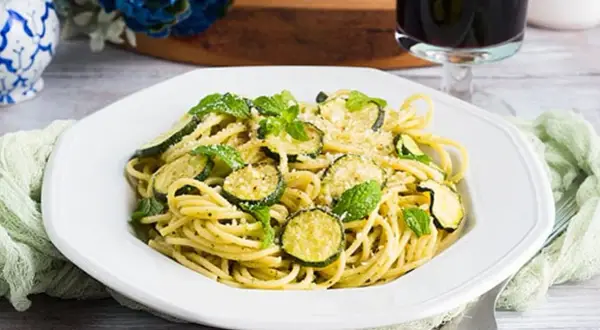 Un piatto di spaghetti con zucchine e menta fresca, un classico della pasta e zucchine alla siciliana, guarnito con parmigiano grattugiato.