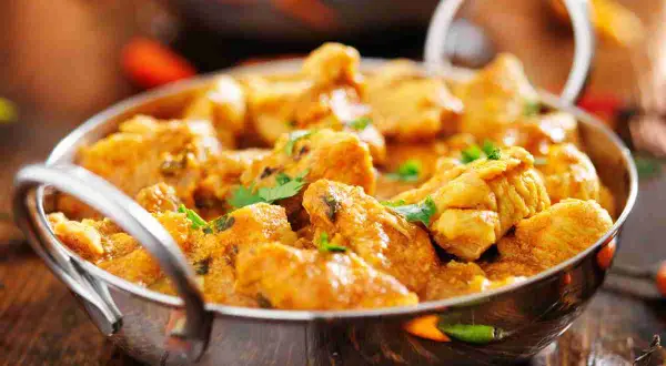 Un invitante pollo al curry cremoso, guarnito con coriandolo fresco, servito in una ciotola metallica su un tavolo di legno.