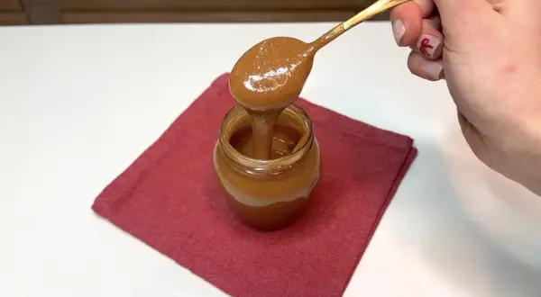 Un cucchiaio d'oro raccoglie un cremoso dulce de leche da un vasetto su un tovagliolo rosso.