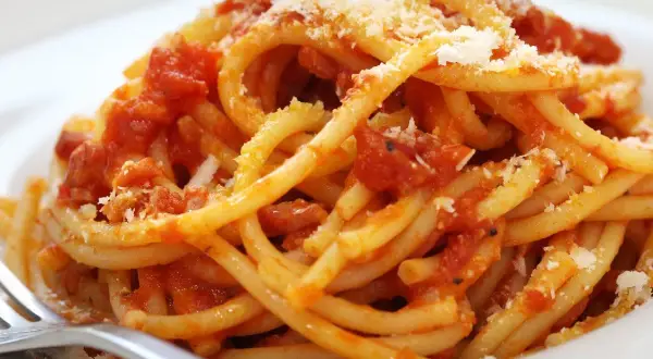 Un piatto di bucatini fumanti conditi con un ricco sugo all'amatriciana ricetta della nonna, spolverato di pecorino.