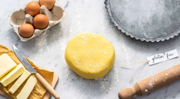 Impasto giallo brillante per pasta frolla senza glutine, pronto per essere steso. Ingredienti freschi e teglia per crostate a portata di mano.