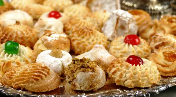 Vassoio pieno di biscotti alle mandorle, alcuni decorati con ciliegie rosse, mandorle e pistacchi.