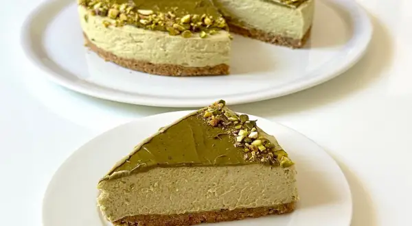 Una fetta di goloso cheesecake al pistacchio, con la torta intera sullo sfondo.