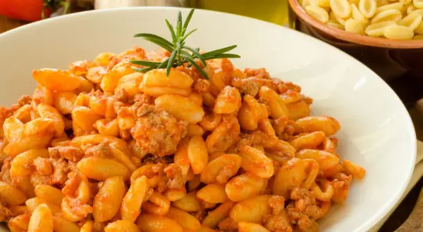 Un piatto invitante di malloreddus alla campidanese, conditi con un ricco sugo di carne e guarniti con rosmarino.