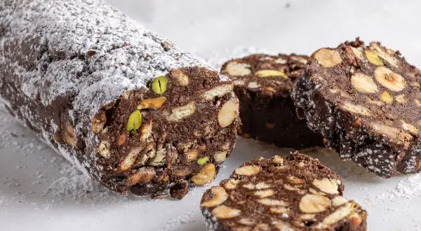 Salame di cioccolato senza uova ricetta della nonna, con biscotti, nocciole e pistacchi, spolverato di zucchero a velo.