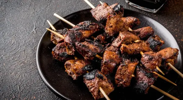 Spiedini di carne succulenti e grigliati, pronti per essere gustati con una salsa scura in un piattino.