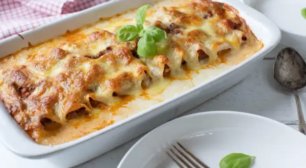 Cannelloni ripieni di carne macinata e mozzarella, cotti al forno e gratinati, guarniti con basilico fresco.