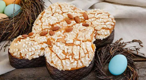 Colomba pasquale con glassa croccante, mandorle e zuccherini, decorata con uova e nidi di Pasqua.