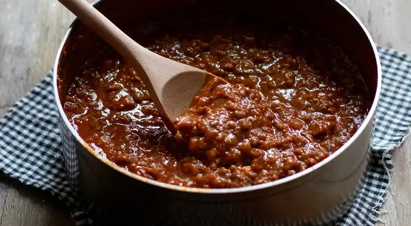 Un pentolone pieno di ragù alla bolognese, pronto per condire la pasta. Un cucchiaio di legno mescola la salsa ricca e saporita.