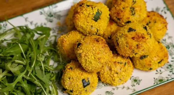 Polpette di zucchine al forno dorate e croccanti, servite su un piatto con rucola fresca.