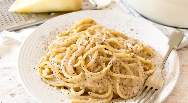 Un piatto di spaghetti fumanti, conditi con la cremosità del cacio e pepe, cosparsi di pepe nero macinato fresco.