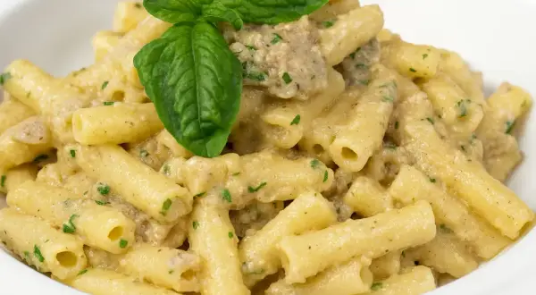 Piatto di pasta con melanzane in bianco, condita con una cremosa salsa e guarnita con basilico fresco.