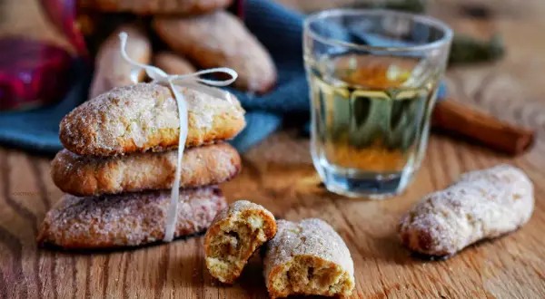 Ciambelline al vino dorate e zuccherate, una invitante pila legata da un nastro bianco, accanto a un bicchierino di vino e cannella.