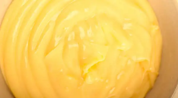 Close-up of smooth, creamy yellow pastry cream in a bowl, with visible swirls and highlights.