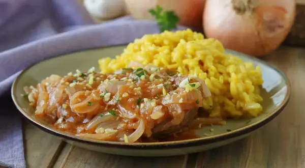 Un succulento ossobuco alla milanese, tenero e saporito, servito con un cremoso risotto giallo.