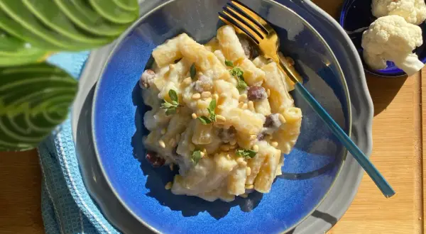 Creamy pasta with cauliflower, pine nuts, and herbs on a blue plate with a gold fork.