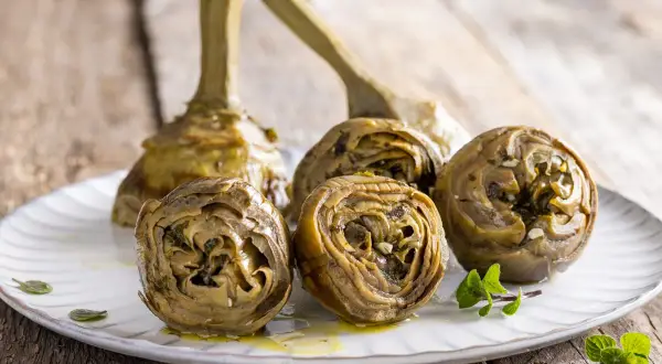 Carciofi alla romana ricetta: carciofi stufati con erbe aromatiche e aglio su un piatto bianco, pronti per essere gustati.
