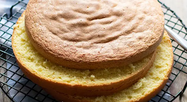 Due dischi di pan di spagna sofficissimo, uno sopra l'altro, su una griglia. La superficie dorata e la mollica gialla invitano a gustarlo.