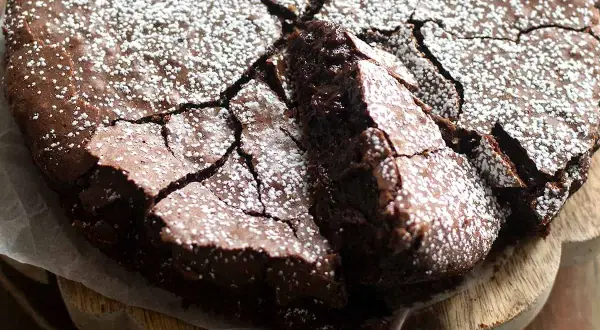 Una deliziosa torta al cioccolato fondente, con una crosta crepata e cosparsa di zucchero a velo, pronta per essere gustata.