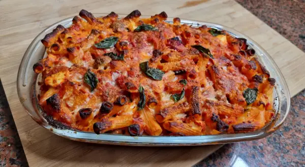 Un invitante piatto di pasta al forno napoletana, con pasta rigata dorata, sugo rosso e formaggio fuso, guarnito con foglie di basilico fresco.