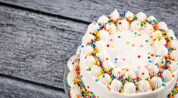 Torta bianca decorata con panna e confettini colorati, un esempio di torte di compleanno particolari per una festa allegra.