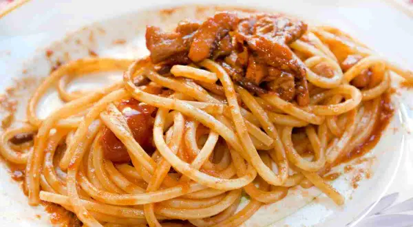 Spaghetti alla chitarra conditi con un ricco sugo di carne e pomodoro, un piatto invitante e saporito.