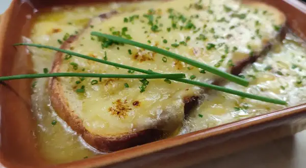 Zuppa di cipolle fumante, con crostini dorati e formaggio filante, guarnita con erba cipollina fresca.