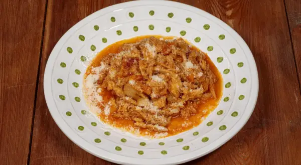 Un piatto di trippa alla fiorentina, saporita e ricca, cosparsa di parmigiano grattugiato, servita su un piatto bianco decorato.