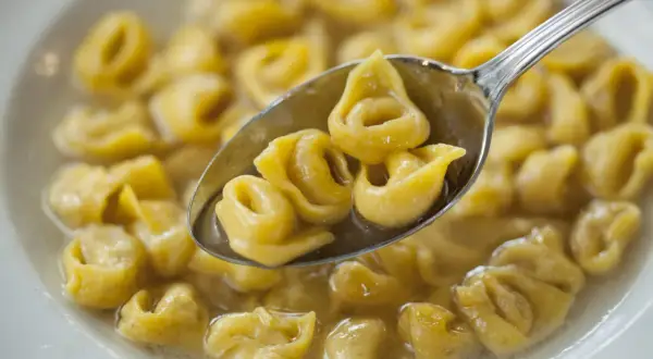 Un cucchiaio raccoglie deliziosi tortellini fatti in casa in brodo, pronti per essere gustati.