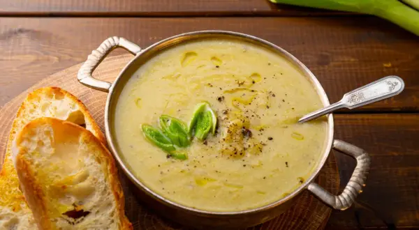 Una ciotola di cremosa crema di patate, guarnita con cipollotto fresco e pepe nero, servita con fette di pane tostato.