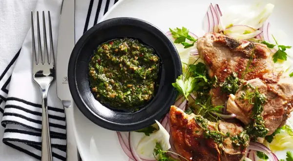 Costolette d'agnello con salsa verde senza uovo, servite su un letto di finocchio e cipolla rossa.