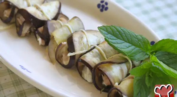 Deliziosi involtini di melanzane ripieni, guarniti con foglie di menta fresca su un piatto bianco.