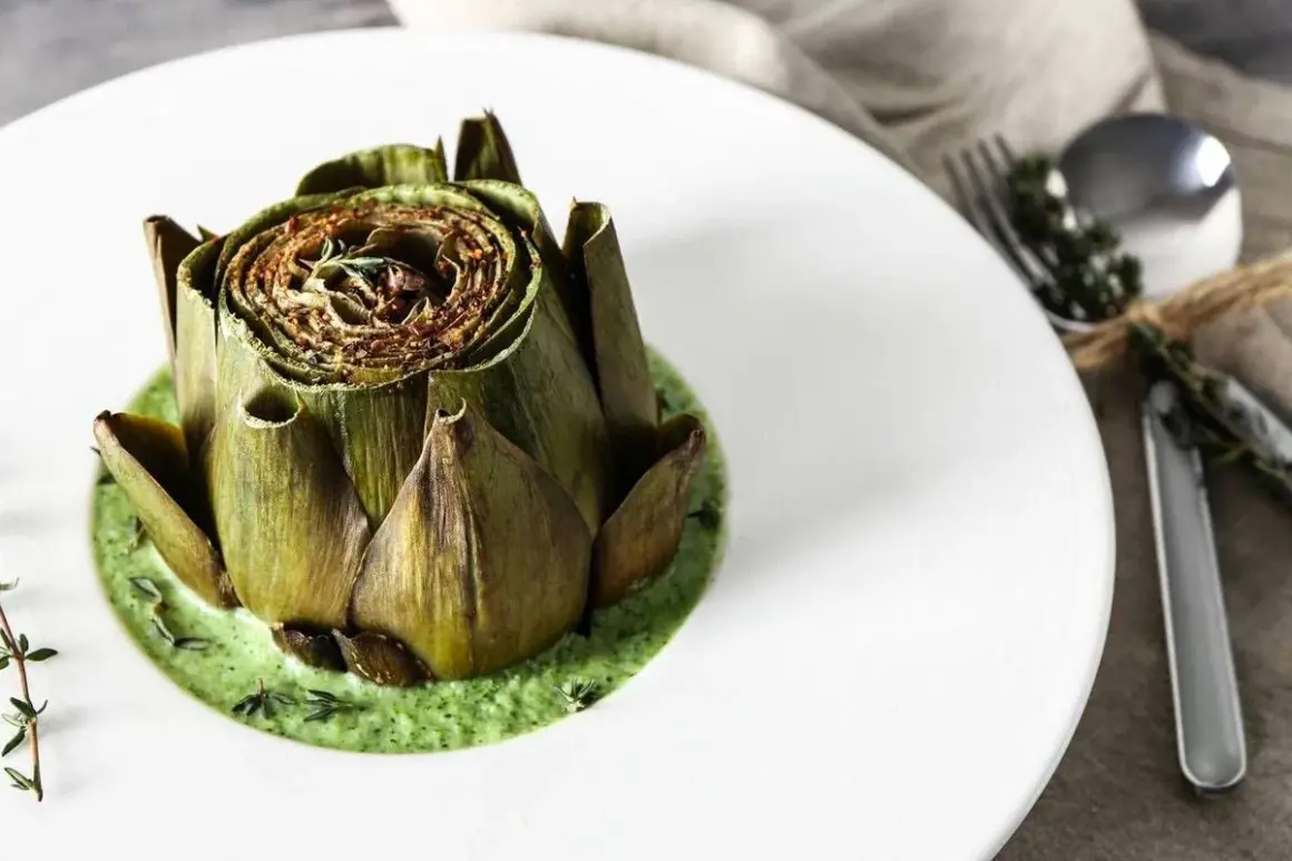 Carciofo intero cotto, adagiato su una vellutata crema di carciofi, guarnito con erbe aromatiche.