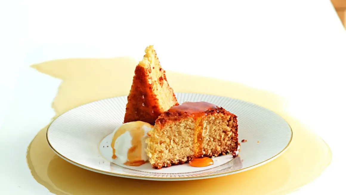 Fetta di torta al cocco con gelato alla vaniglia e sciroppo dorato.