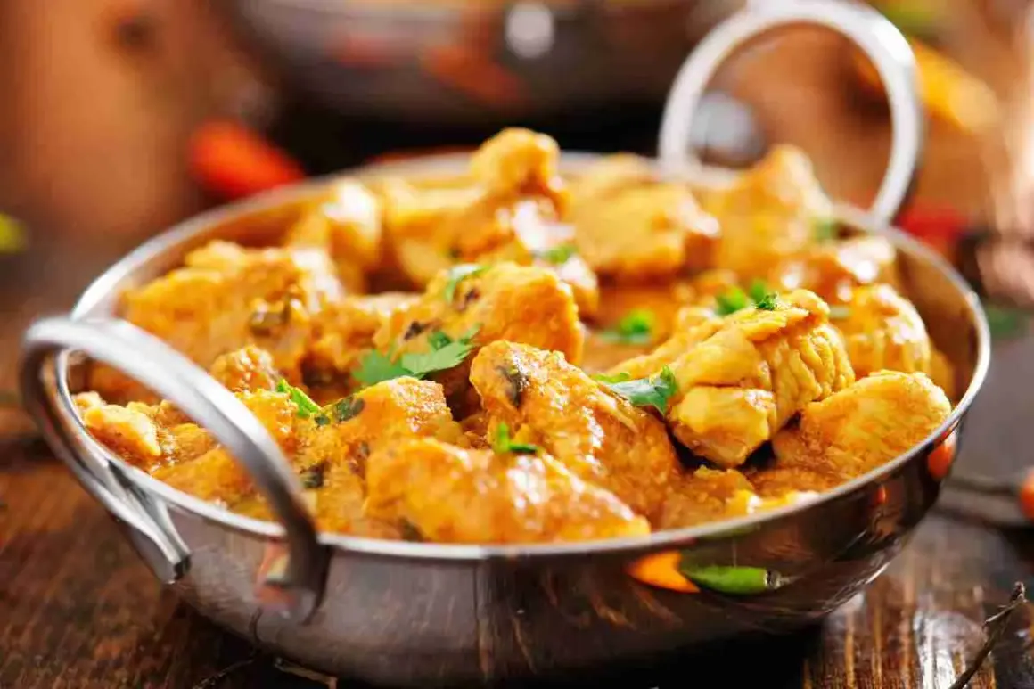 Un invitante pollo al curry cremoso, guarnito con coriandolo fresco, servito in una ciotola metallica su un tavolo di legno.