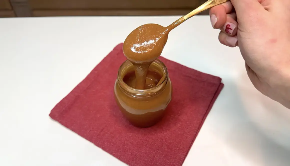 Un cucchiaio d'oro raccoglie un cremoso dulce de leche da un vasetto su un tovagliolo rosso.