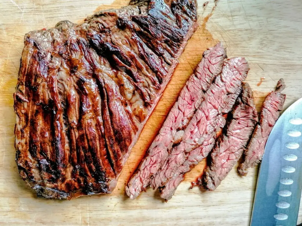 Diaframma di manzo grigliato, tagliato a fette sottili su un tagliere di legno. La carne è succulenta e ben cotta, con striature di grasso che la rendono ancora più invitante.