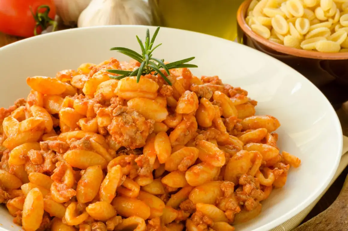 Un piatto invitante di malloreddus alla campidanese, conditi con un ricco sugo di carne e guarniti con rosmarino.