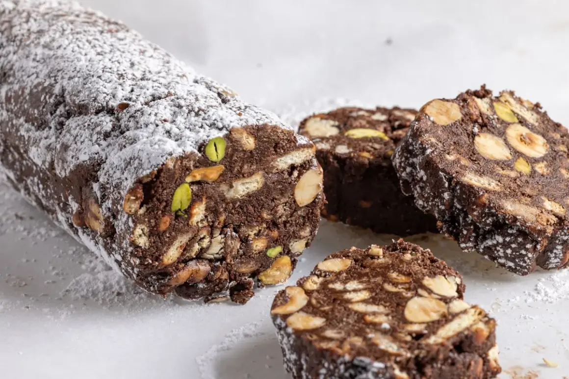 Salame di cioccolato senza uova ricetta della nonna, con biscotti, nocciole e pistacchi, spolverato di zucchero a velo.