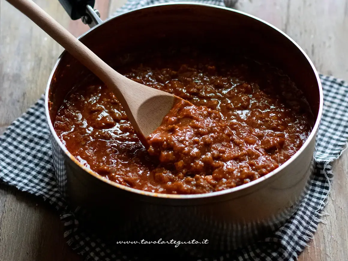 Un pentolone pieno di ragù alla bolognese, pronto per condire la pasta. Un cucchiaio di legno mescola la salsa ricca e saporita.